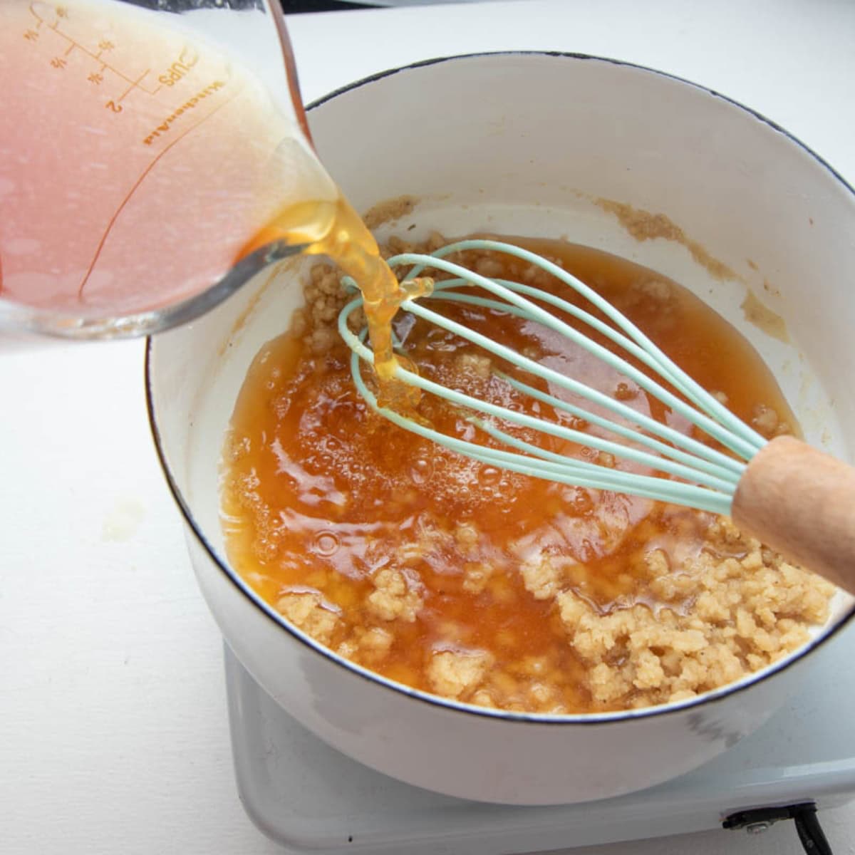 Broth pours over a whisk and into a pot holding a roux.