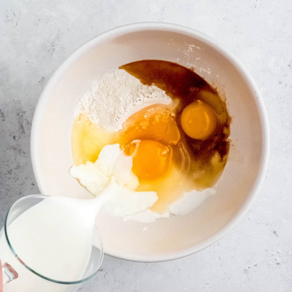Milk pours into a bowl of ingredients for pannukakku.