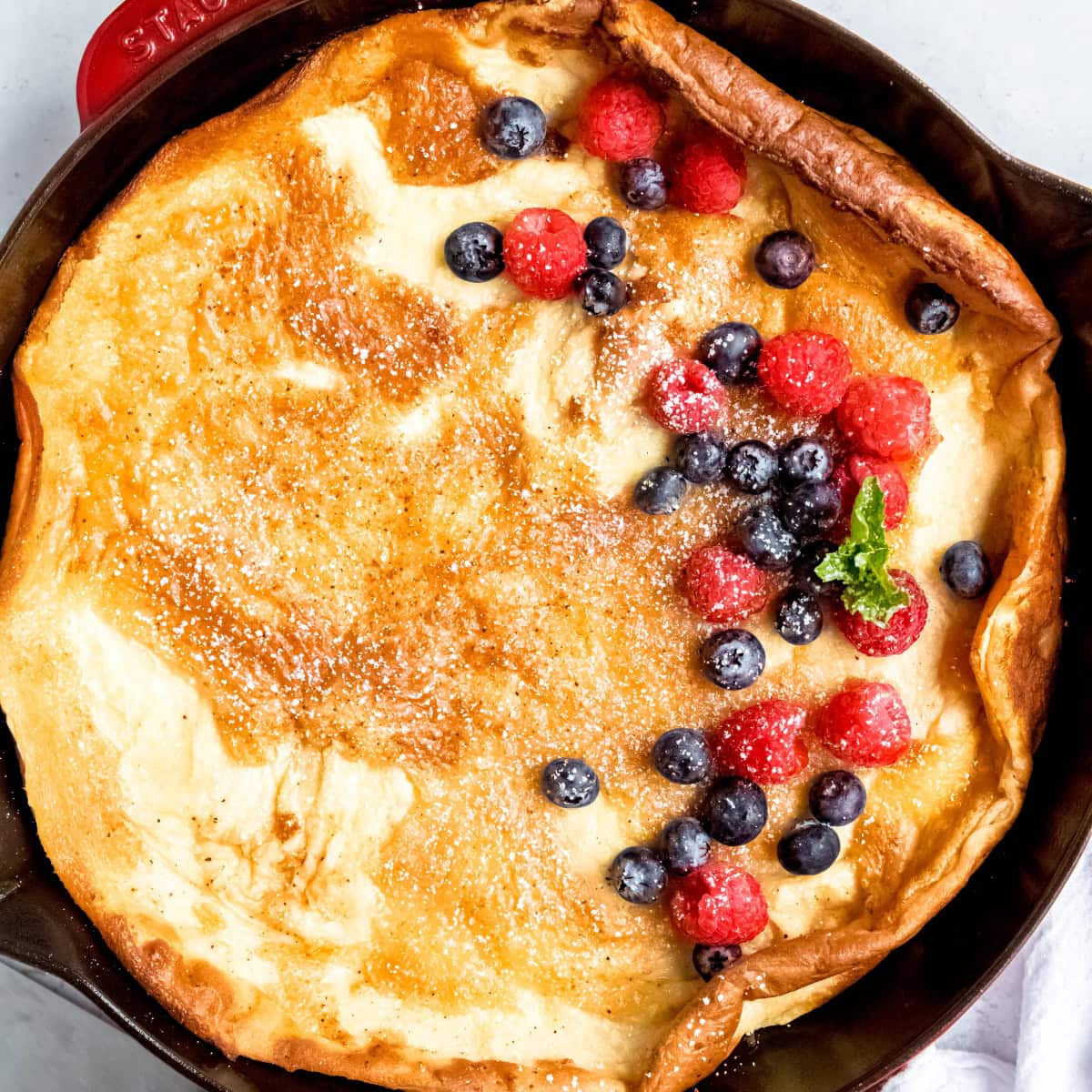 A baked pannukakku topped with berries, powdered sugar, and a sprig of mint.