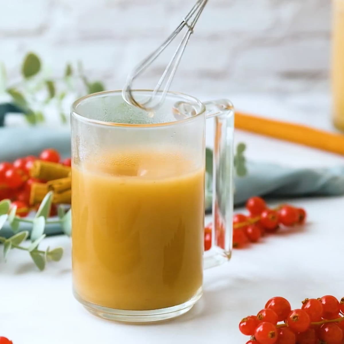 A whisk stirs rum into a glass mug of hot buttered rum.