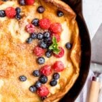 Pannukakku curling up at the edges, garnished with berries and powdered sugar.