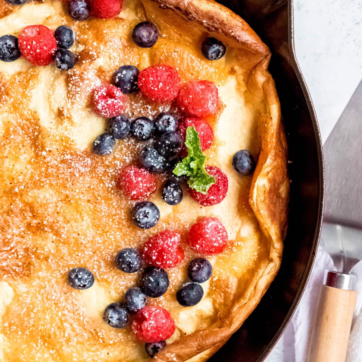 Pannukakku curling up at the edges, garnished with berries and powdered sugar.
