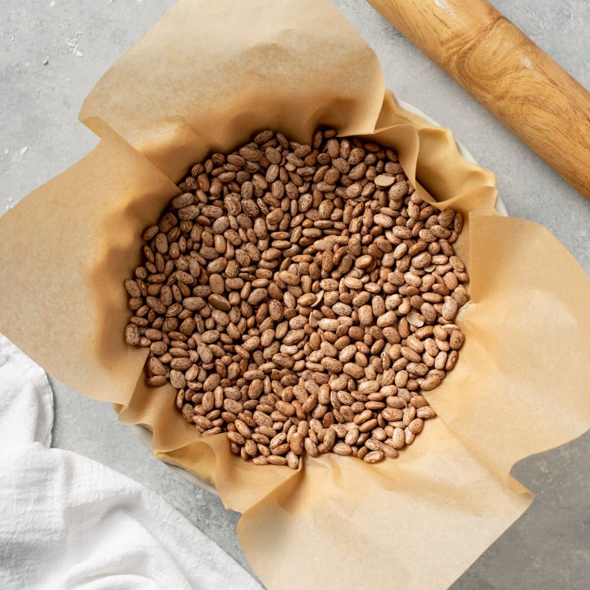 A pie crust lined with parchment paper, filled with dry beans.