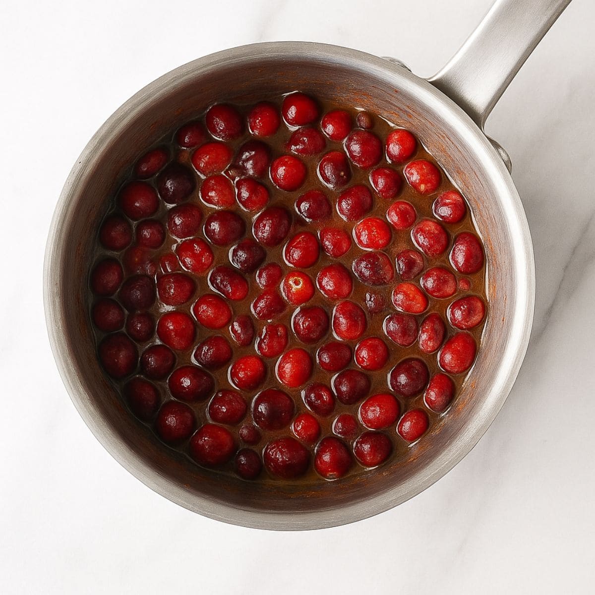 Cranberry orange sauce comes to a boil in a steel saucepan.