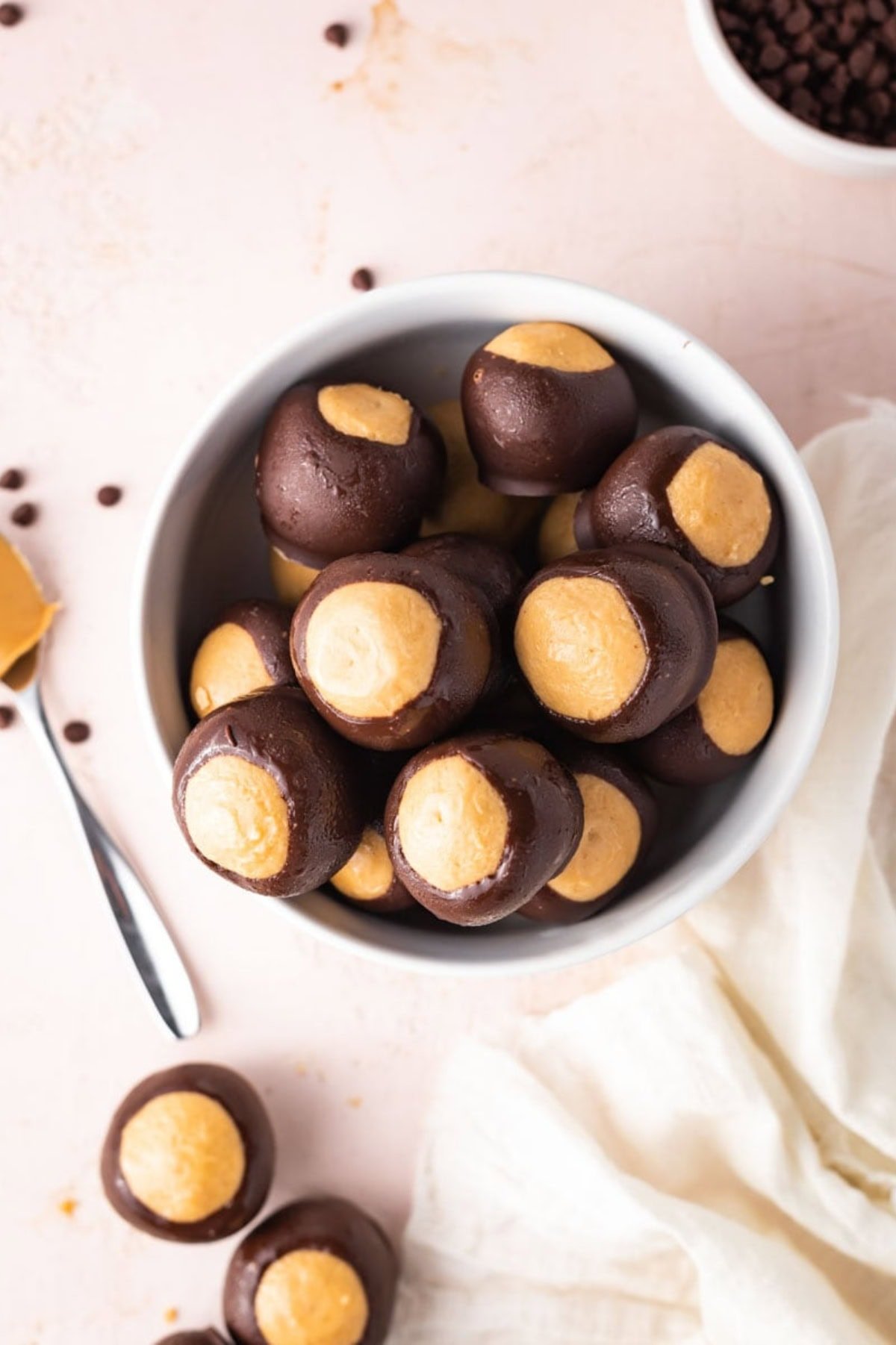 A bowl full of homemade buckeye balls, with a spoon of peanut butter nearby.