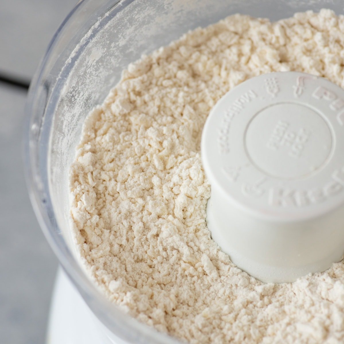 A food processor filled with the crumbly starts of an all-butter pie crust.