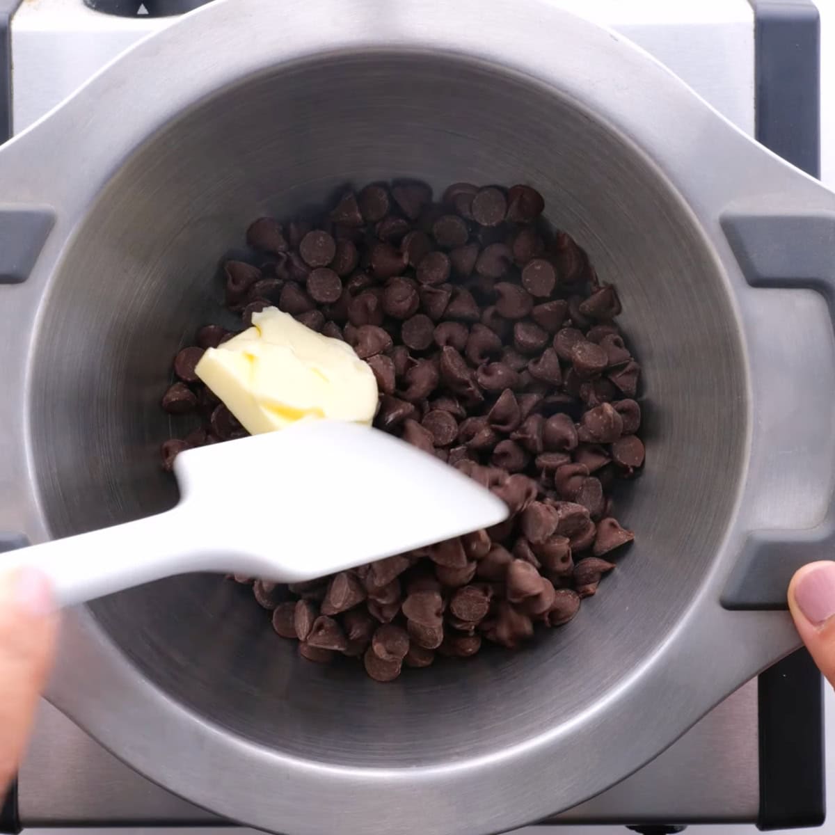 A white rubber spatula stirs butter and chocolate chips together in a double boiler.