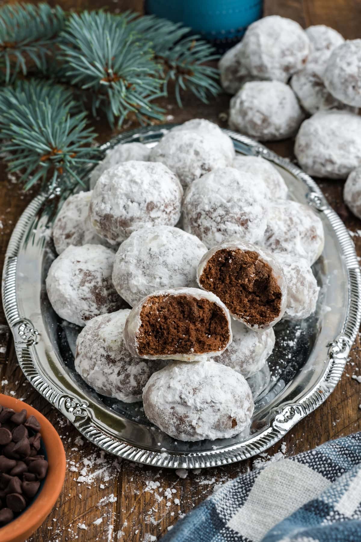 A silver plate of chocolate snowball cookies on a dark wooden table.
