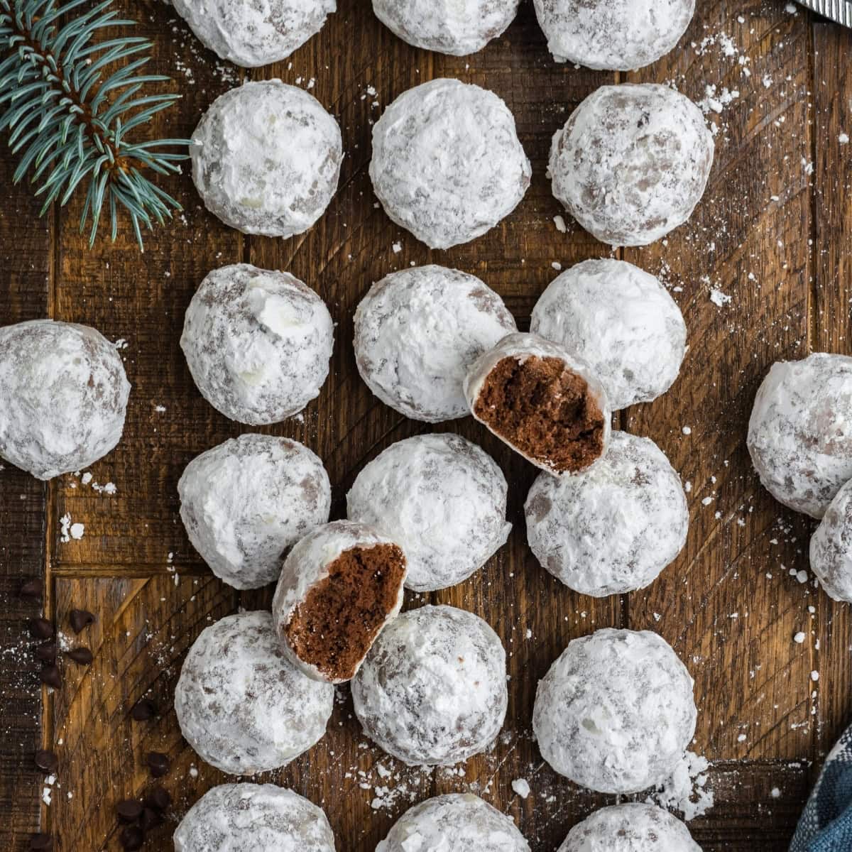 Chocolate snowball cookies laid out in rows on a dark wooden table.