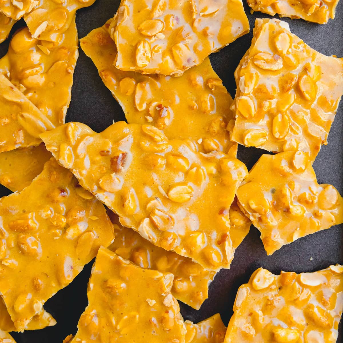 Broken up homemade peanut brittle on a baking sheet.