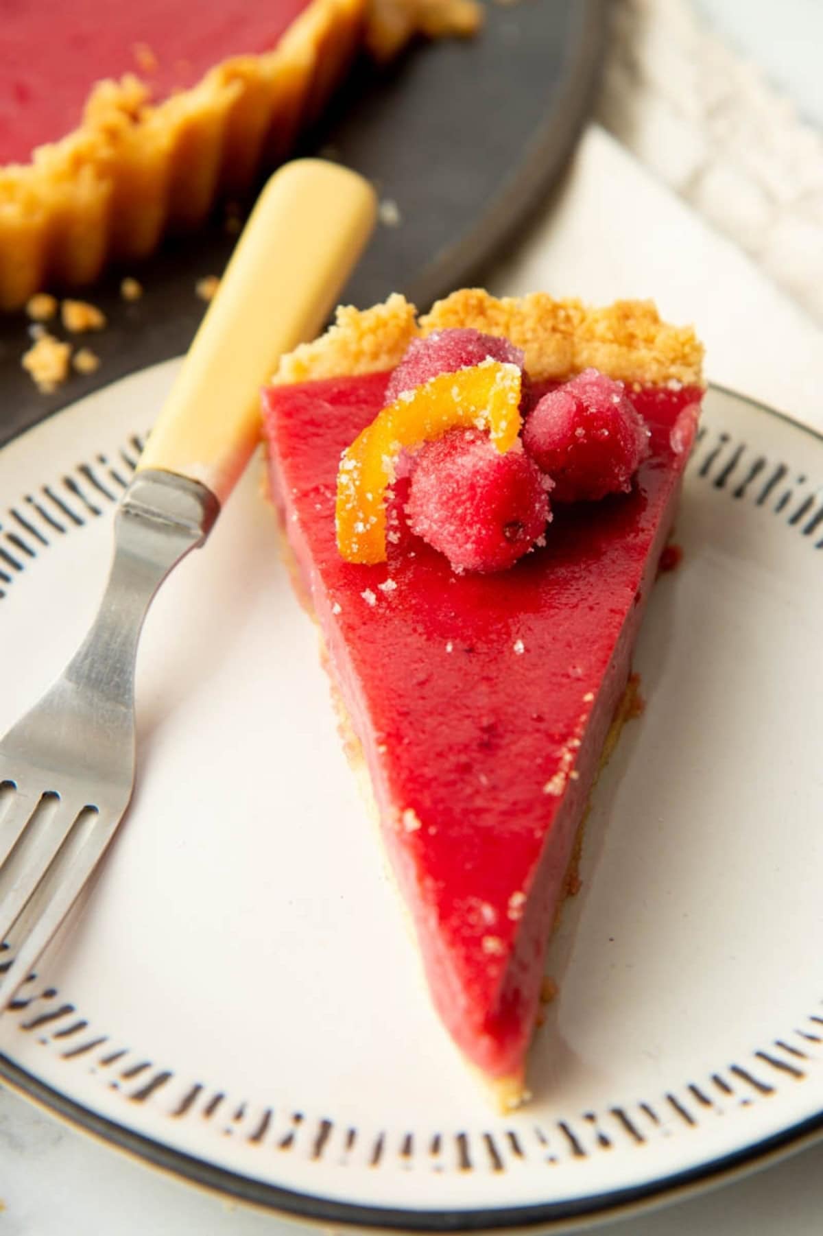 A slice of cranberry curd tart on a plate with a fork.