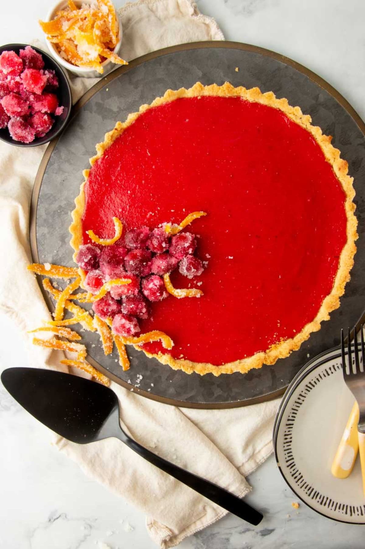 A cranberry curd tart garnished with candied orange peel and sugared cranberries.
