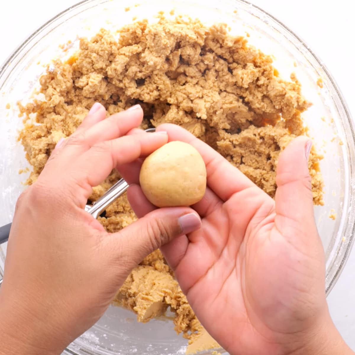 Hands roll a peanut butter ball over a bowl of peanut butter candy mixture.