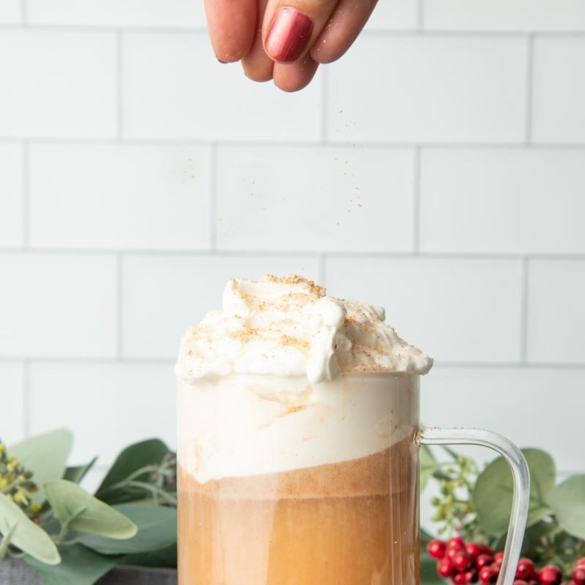 A hand sprinkles fresh nutmeg over a mug of hot buttered rum.