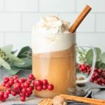 A glass mug of hot buttered rum, garnished with whipped cream and a cinnamon stick.