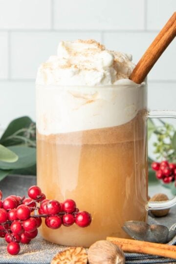 A glass mug of hot buttered rum, garnished with whipped cream and a cinnamon stick.