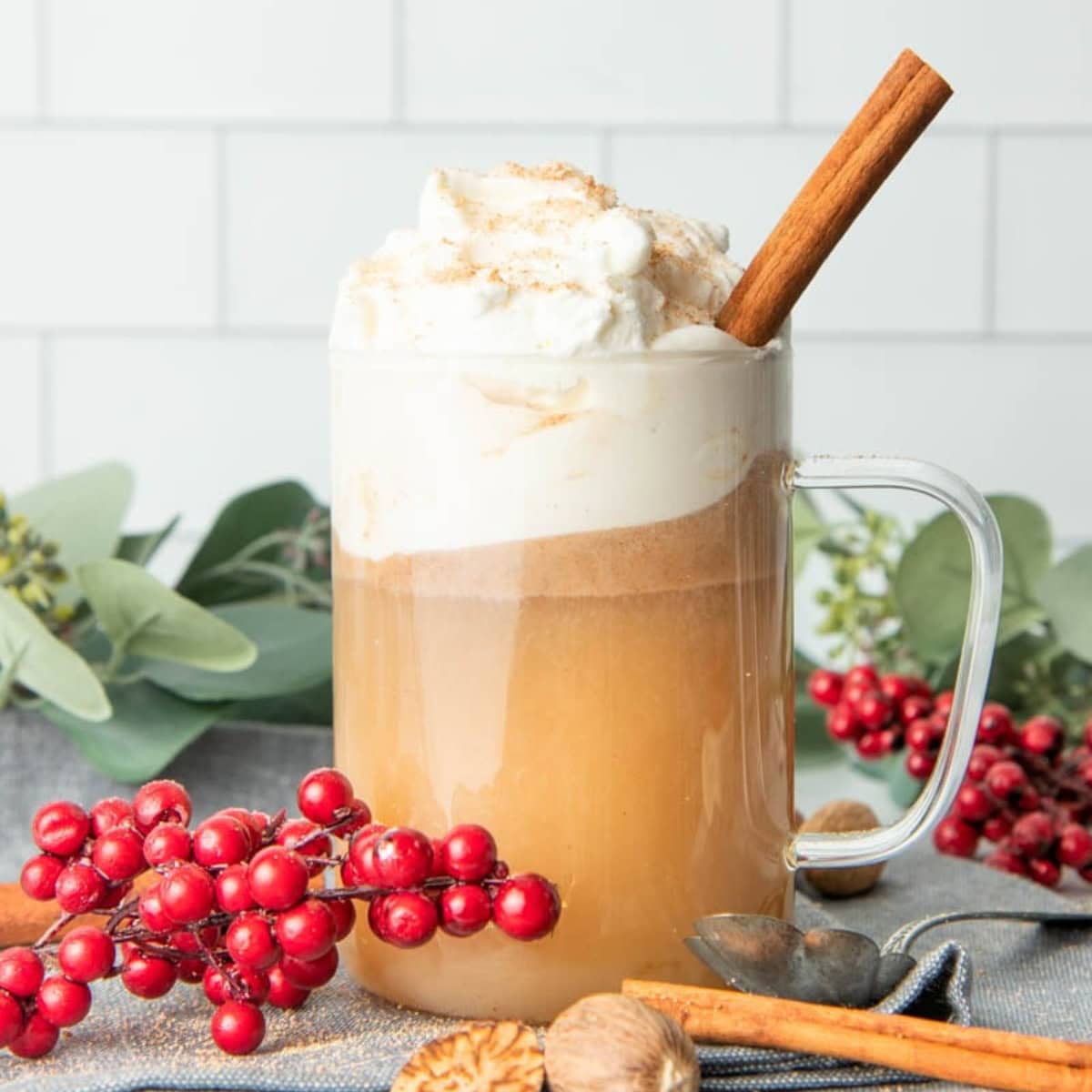A glass mug of hot buttered rum, garnished with whipped cream and a cinnamon stick.
