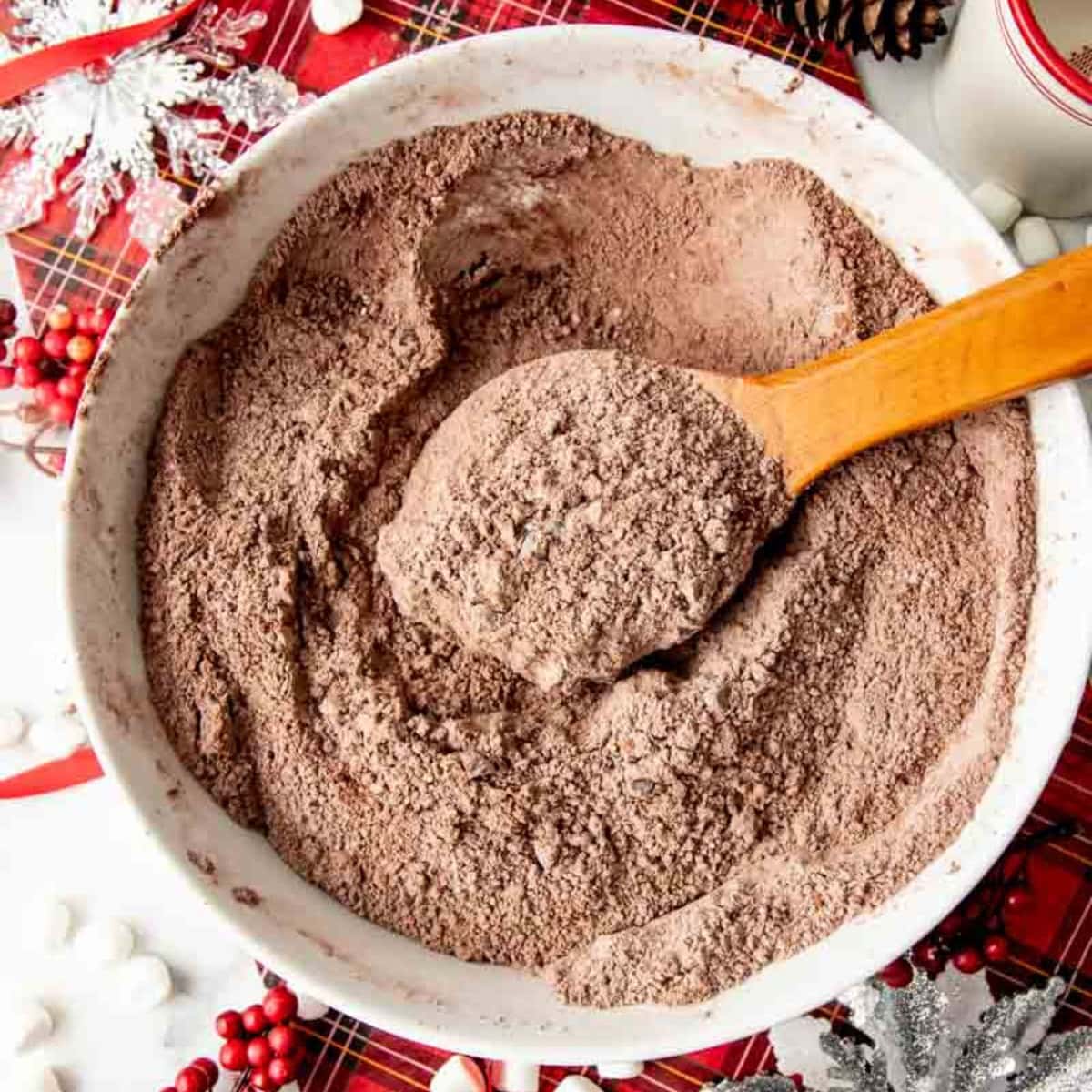 A wooden spoon in a white mixing bowl of hot chocolate mix.