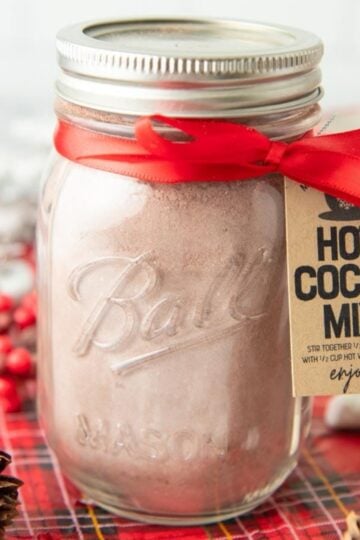 A jar of hot chocolate mix tied with a red ribbon with a kraft paper tag.