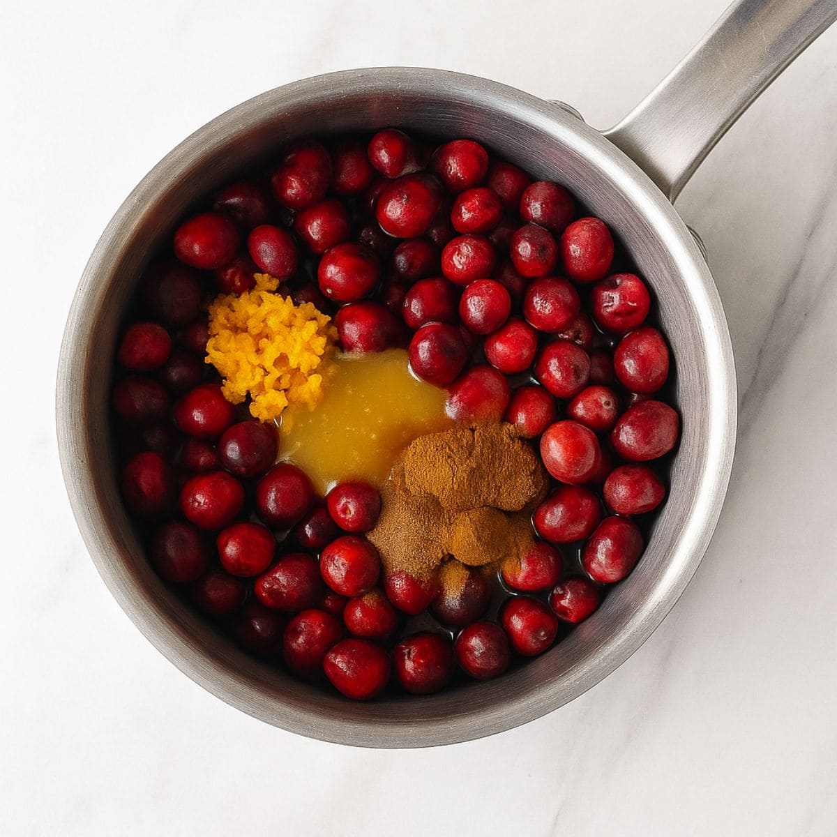Ingredients for cranberry orange sauce in a stainless steel saucepan.