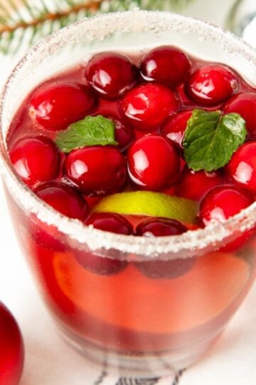 A glass of jingle juice with a sparkly sugar rim, whole cranberries, and fresh mint leaves.
