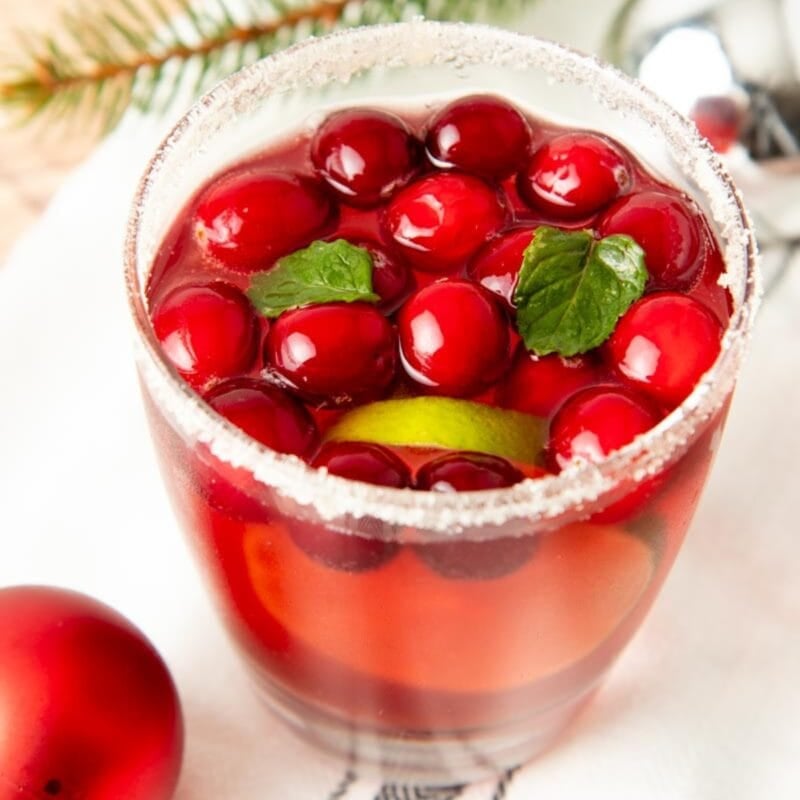 A glass of jingle juice with a sparkly sugar rim, whole cranberries, and fresh mint leaves.