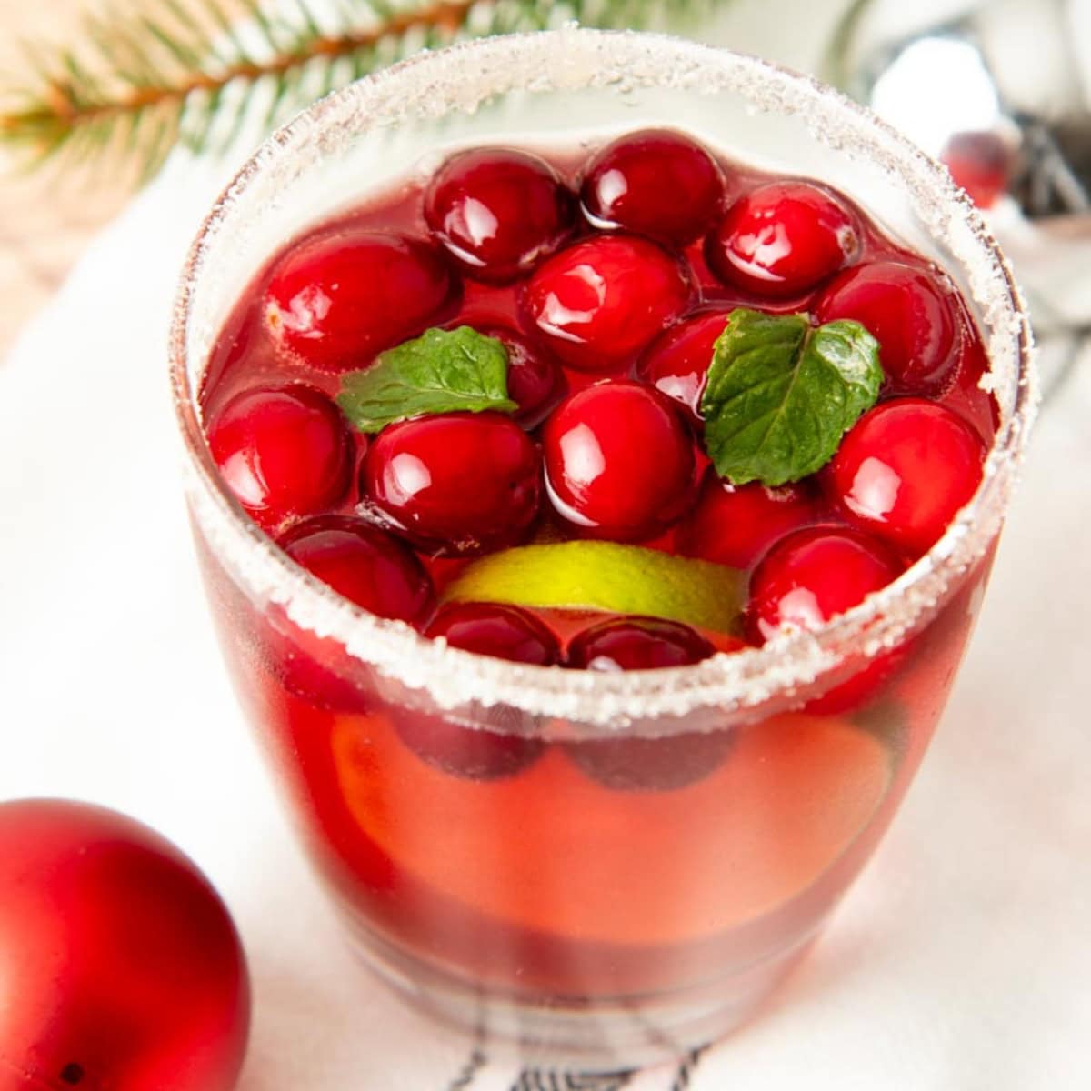 A glass of jingle juice with a sparkly sugar rim, whole cranberries, and fresh mint leaves.