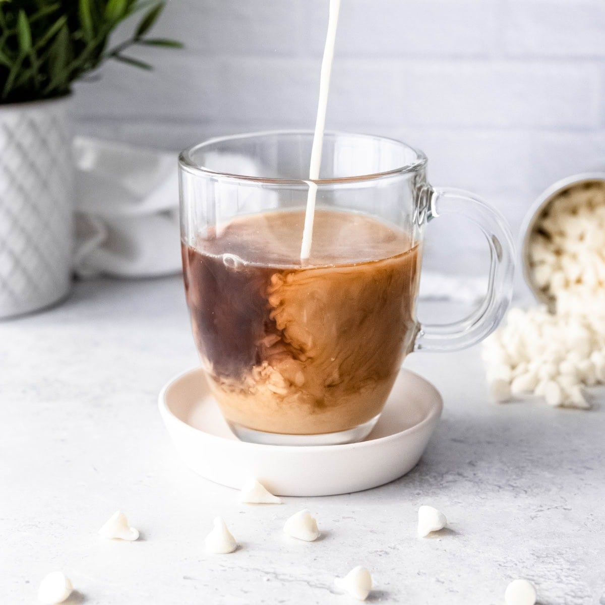 White chocolate milk pours into espresso in a glass mug.
