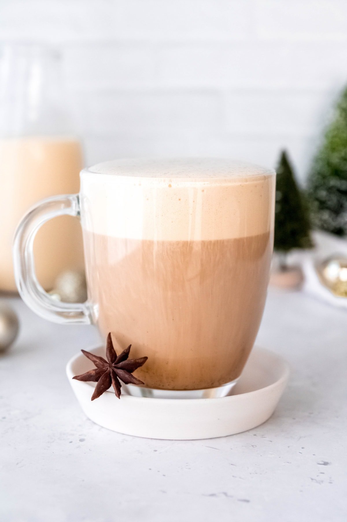 A glass mug of eggnog latte next to a star anise.