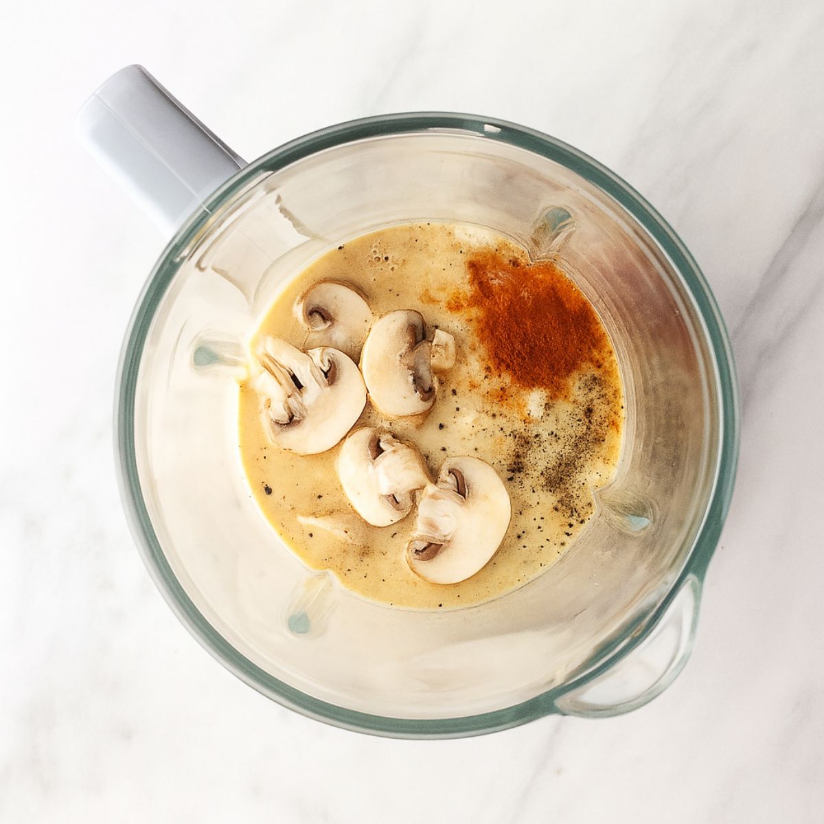 Mushrooms and other sauce ingredients in the basin of a blender.