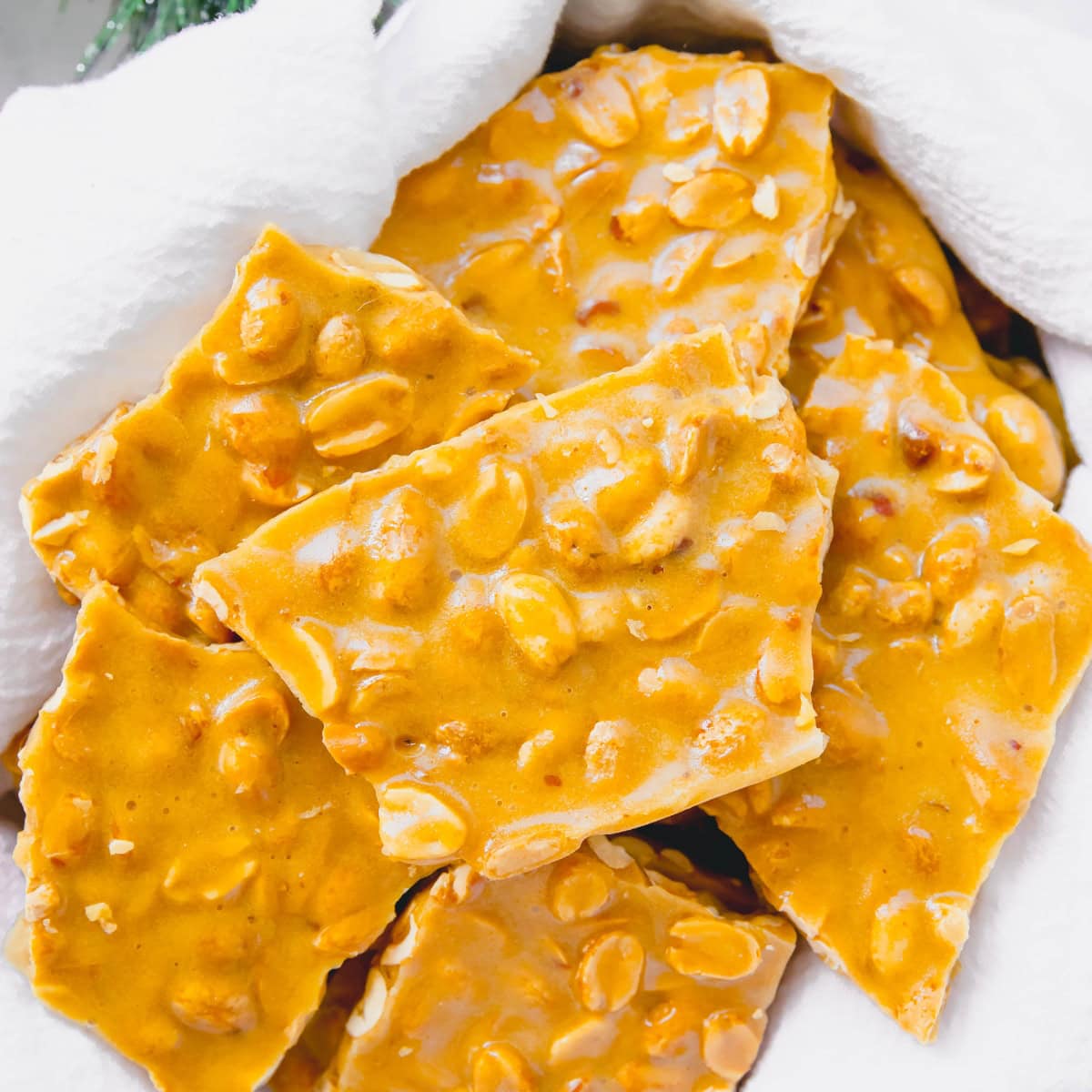 A pile of homemade peanut brittle on a white tea towel.