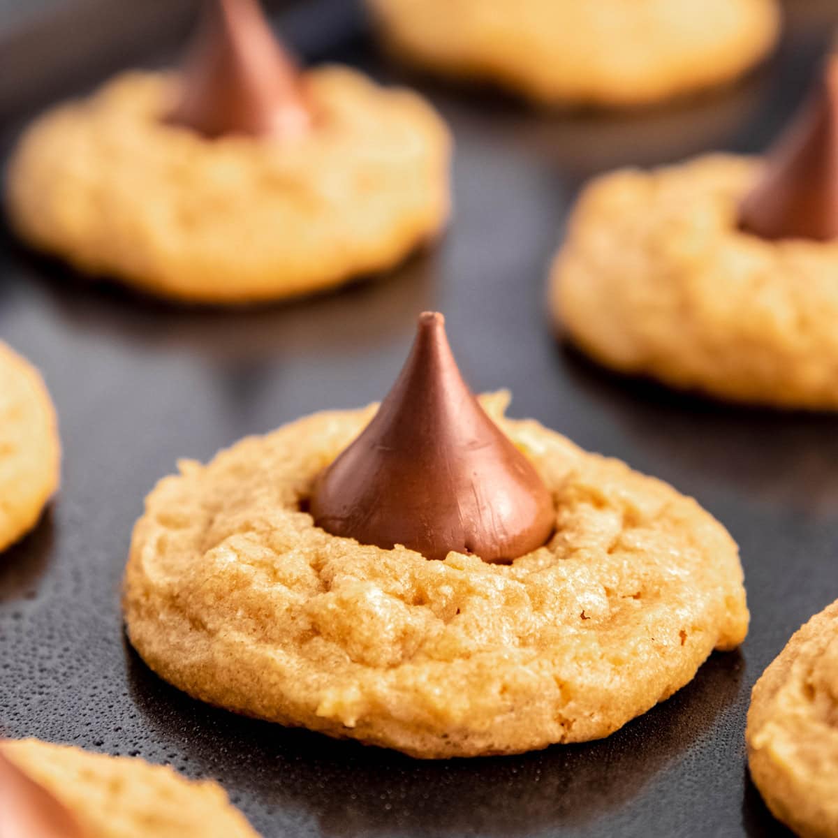 Peanut butter kiss cookies on a dark gray baking sheet.