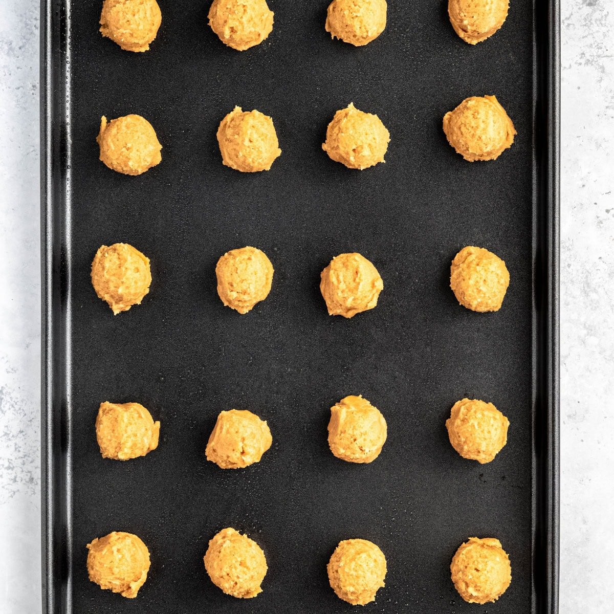 Balls of peanut butter cookie dough in a grid on a baking sheet.