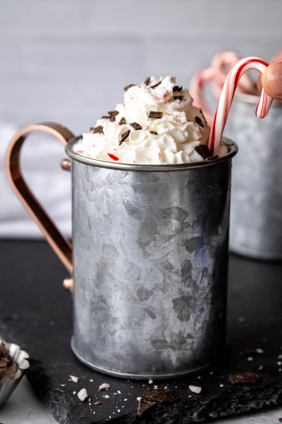 A candy cane sticks out of a tin mug of peppermint mocha.