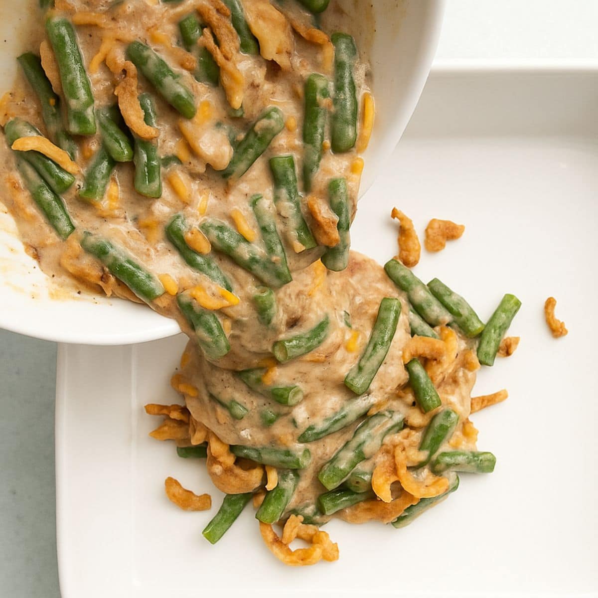 Fresh green bean casserole pours into a white casserole dish.