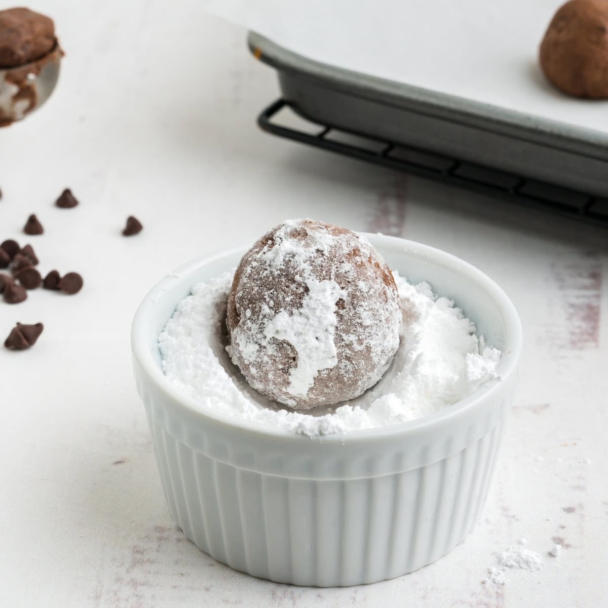 A chocolate ball cookie gets rolled in a small dish of powdered sugar.