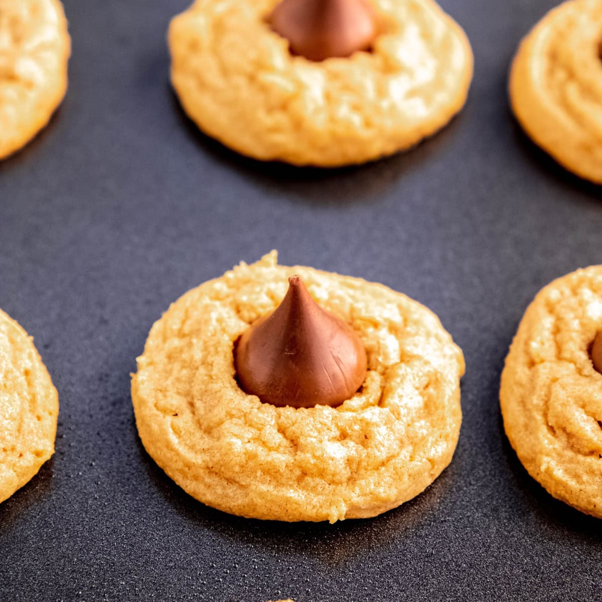 A half dozen peanut butter kiss cookies arranged on a dark gray tray.