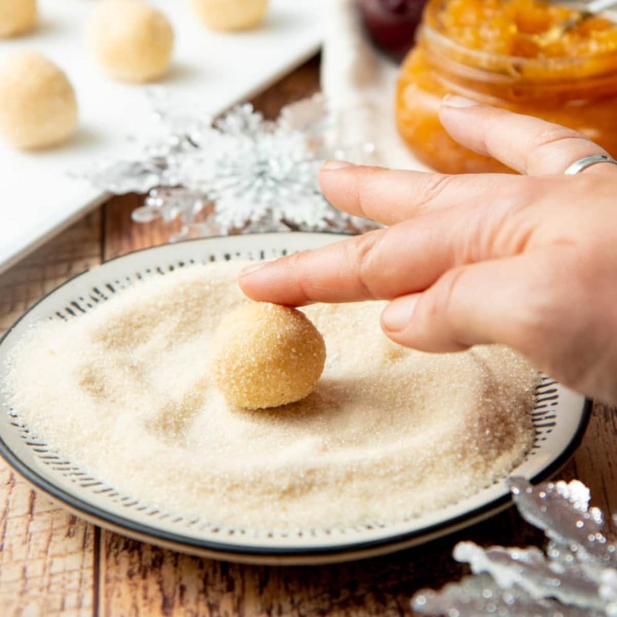 A hand rolls a ball of cookie dough in a plate of sugar.