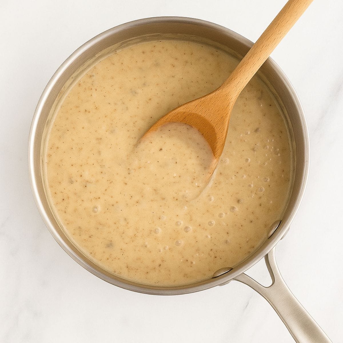 A wooden spoon in a bubbling pot of thickened mushroom sauce for a fresh green bean casserole recipe.