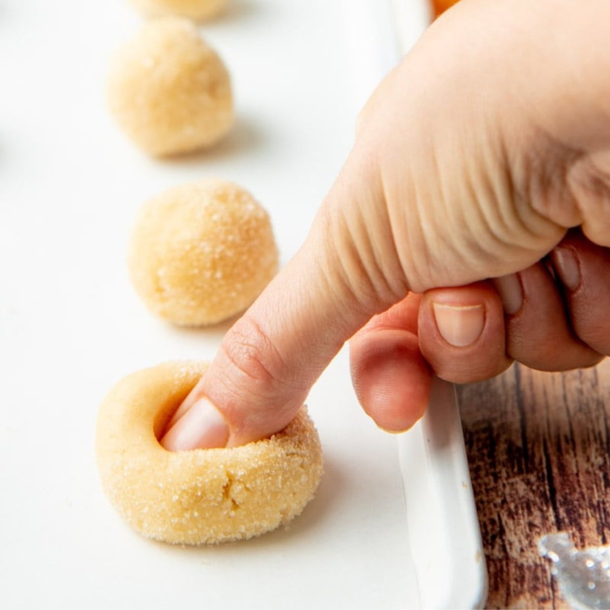 A thumb presses an indent into a ball of cookie dough.