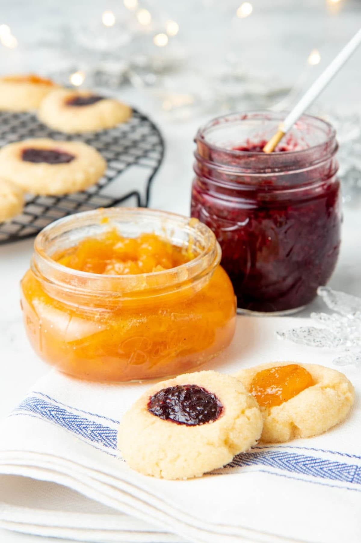 Two jars of jam surrounded by thumbprint cookies with jam.