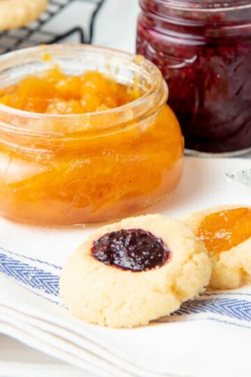 Two thumbprint cookies with jam - one with peach and one with raspberry.