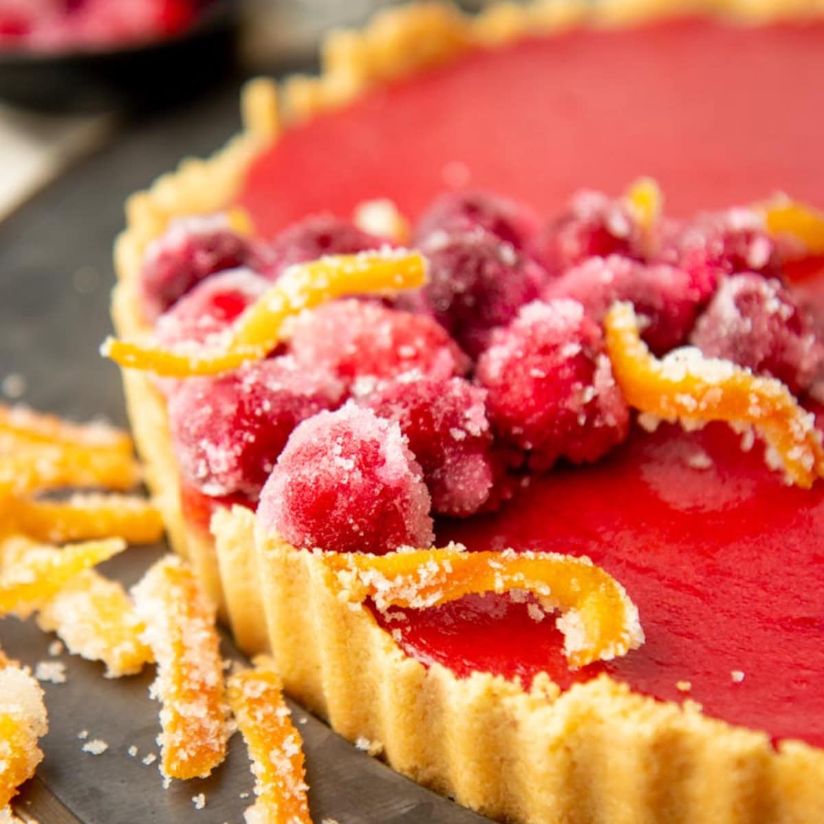 Candied orange peel and sugared strawberries on top of a ruby red cranberry tart.