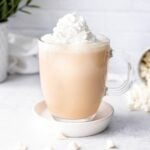 Whipped cream garnishes a white mocha in a glass mug.