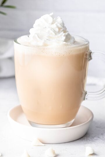 Whipped cream garnishes a white mocha in a glass mug.