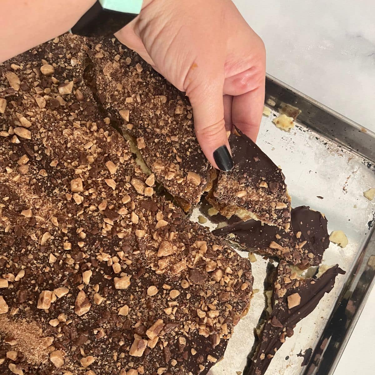 A hand breaks a sheet of saltine cracker toffee into pieces.