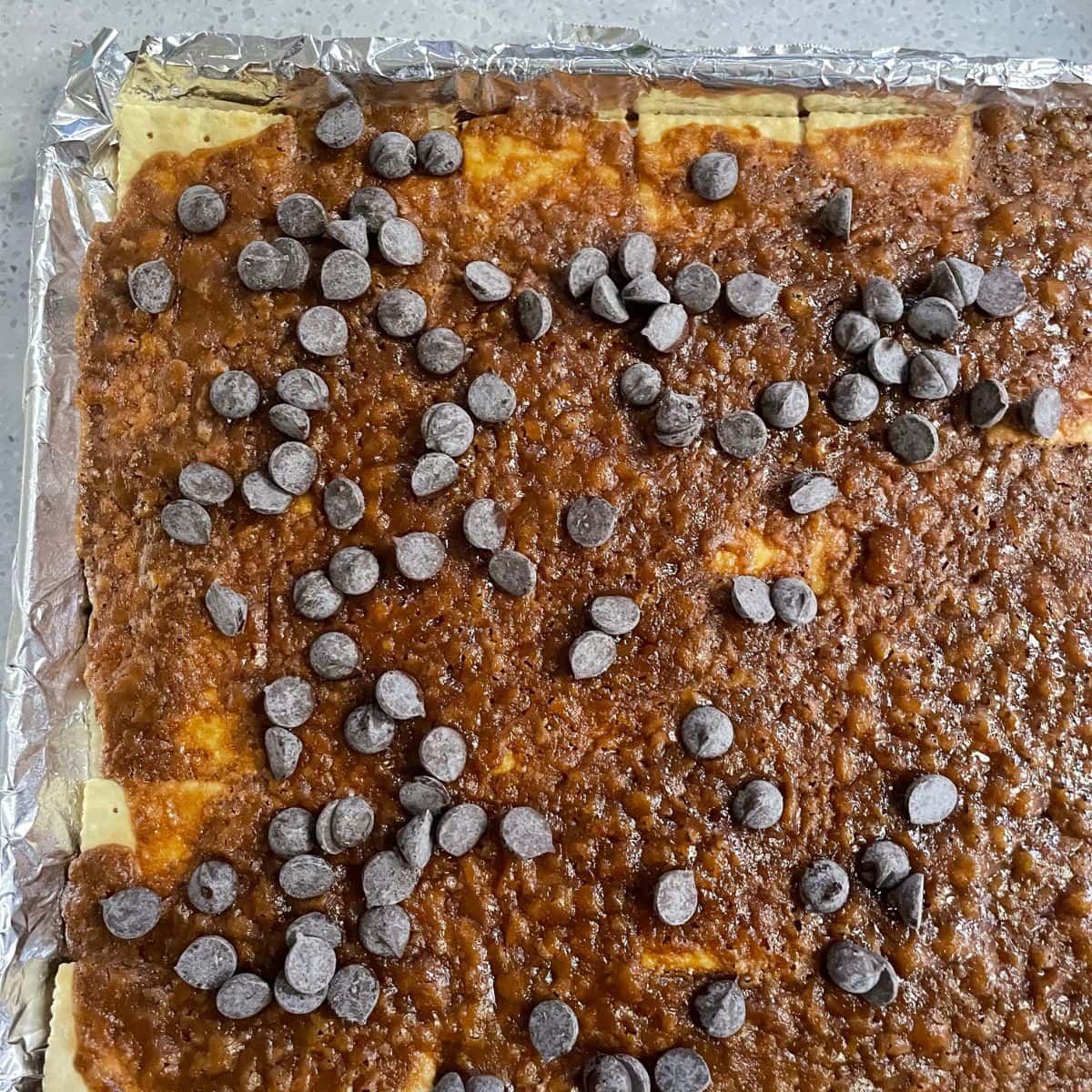 Chocolate chips sprinkled over baked saltine cracker toffee.