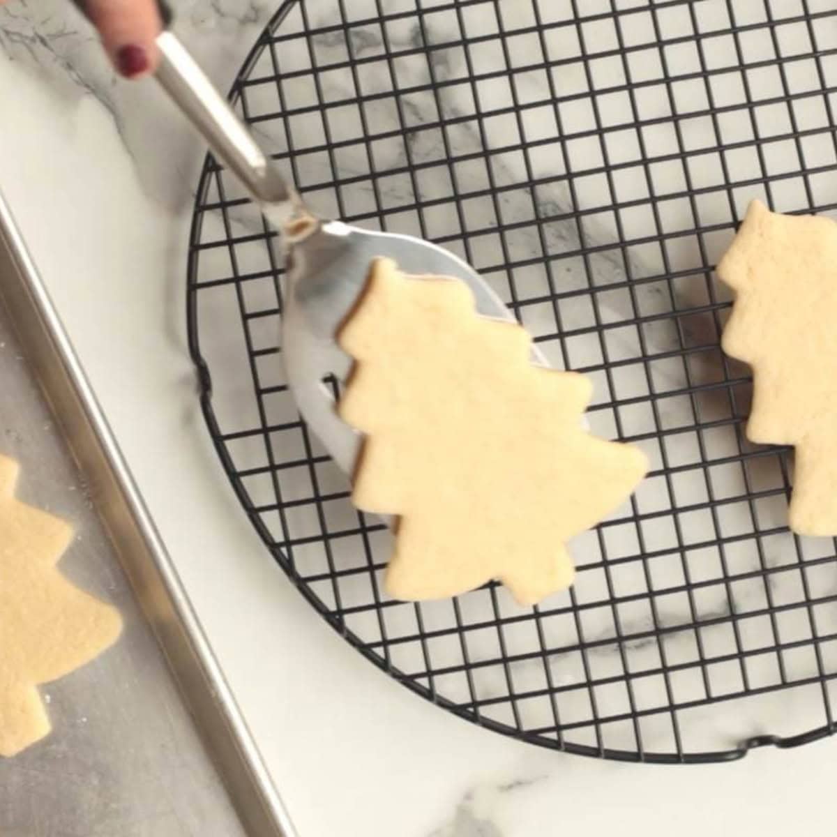 A metal spatula moves a cut-out cookie to a cooling rack.