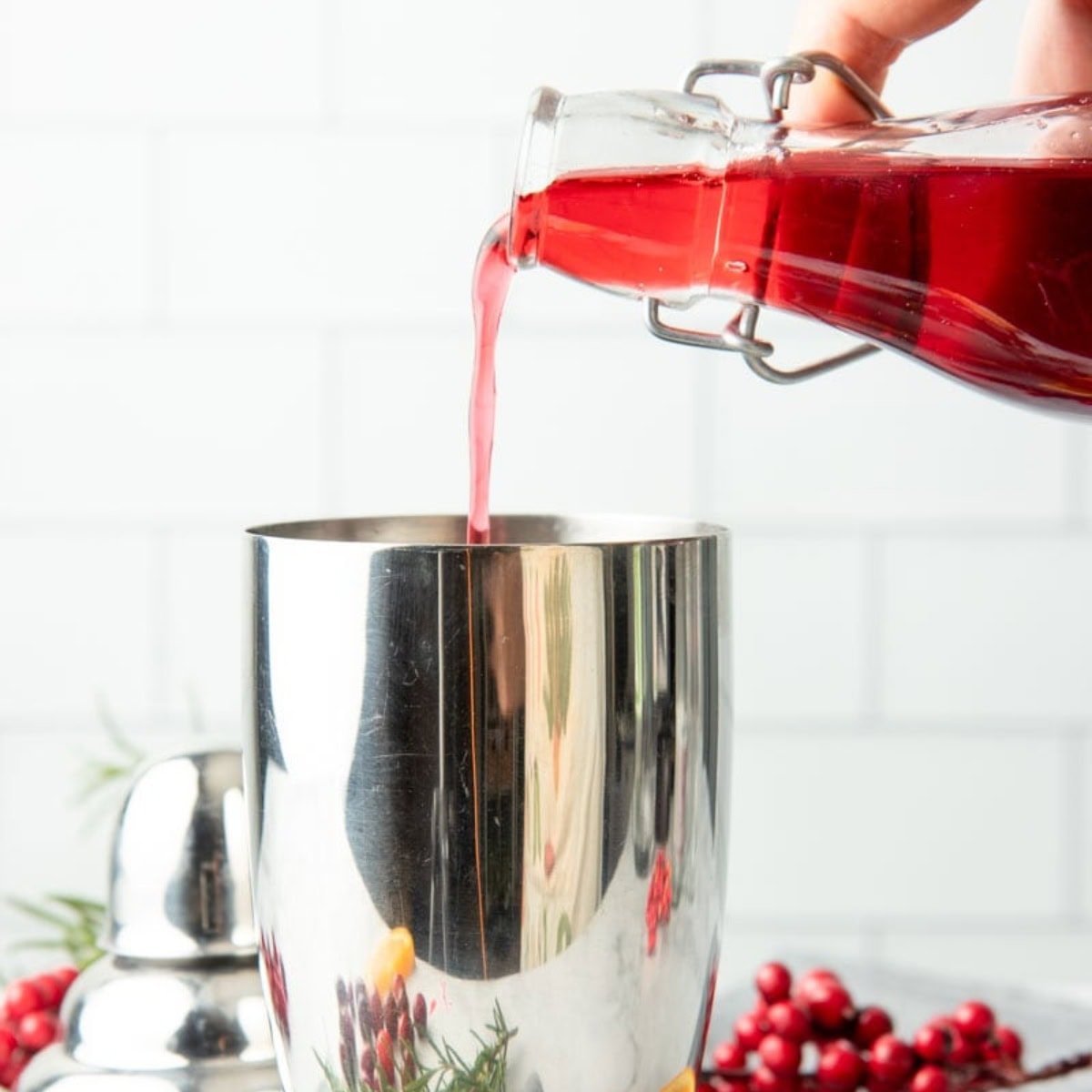 Cranberry simple syrup pours into a silver cocktail shaker.
