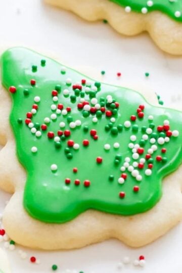 A cut-out sugar cookie decorated with green frosting and red, white, and green sprinkles.